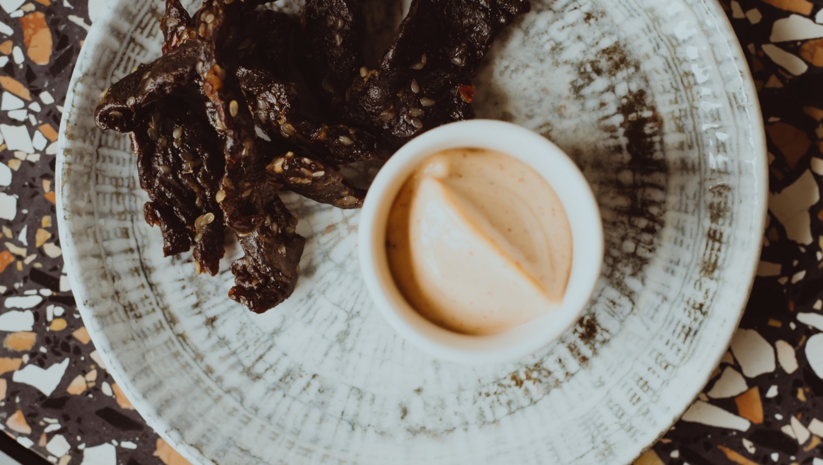 Kawałki marynowanego mięsa podane z kremowym, przyprawionym sosem na ceramicznym talerzu