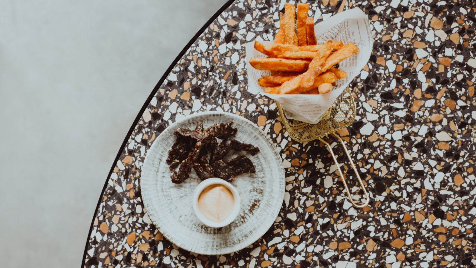 Chrupiące frytki w metalowym koszyku i talerz z chrupiącym mięsem oraz sosem na marmurowym stole w restauracji