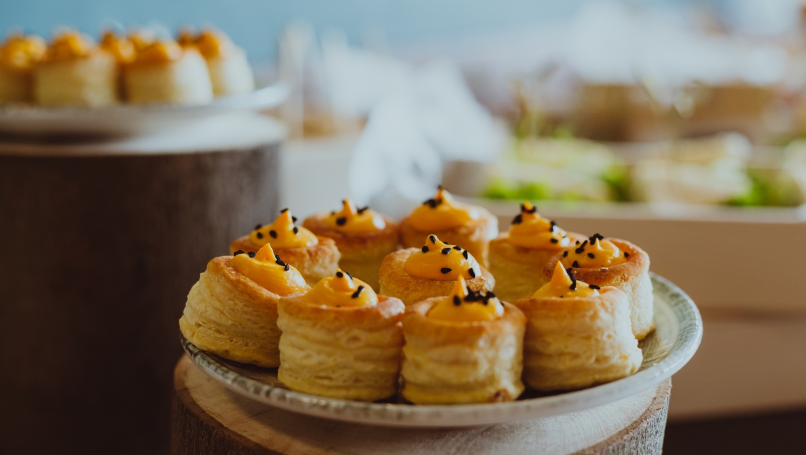 Talerz z delikatnymi, maślanymi ciastkami francuskimi wypełnionymi kremem z żółtym nadzieniem i posypanymi czarnym sezamem