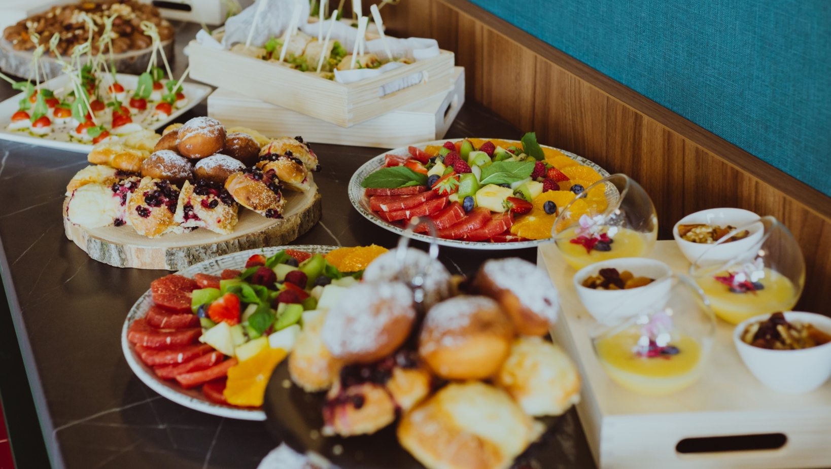 Kolacja bufetowa z różnorodnymi słodkimi wypiekami, świeżymi owocami i stylowymi deserami podanymi na drewnianych i porcelanowych półmiskach.