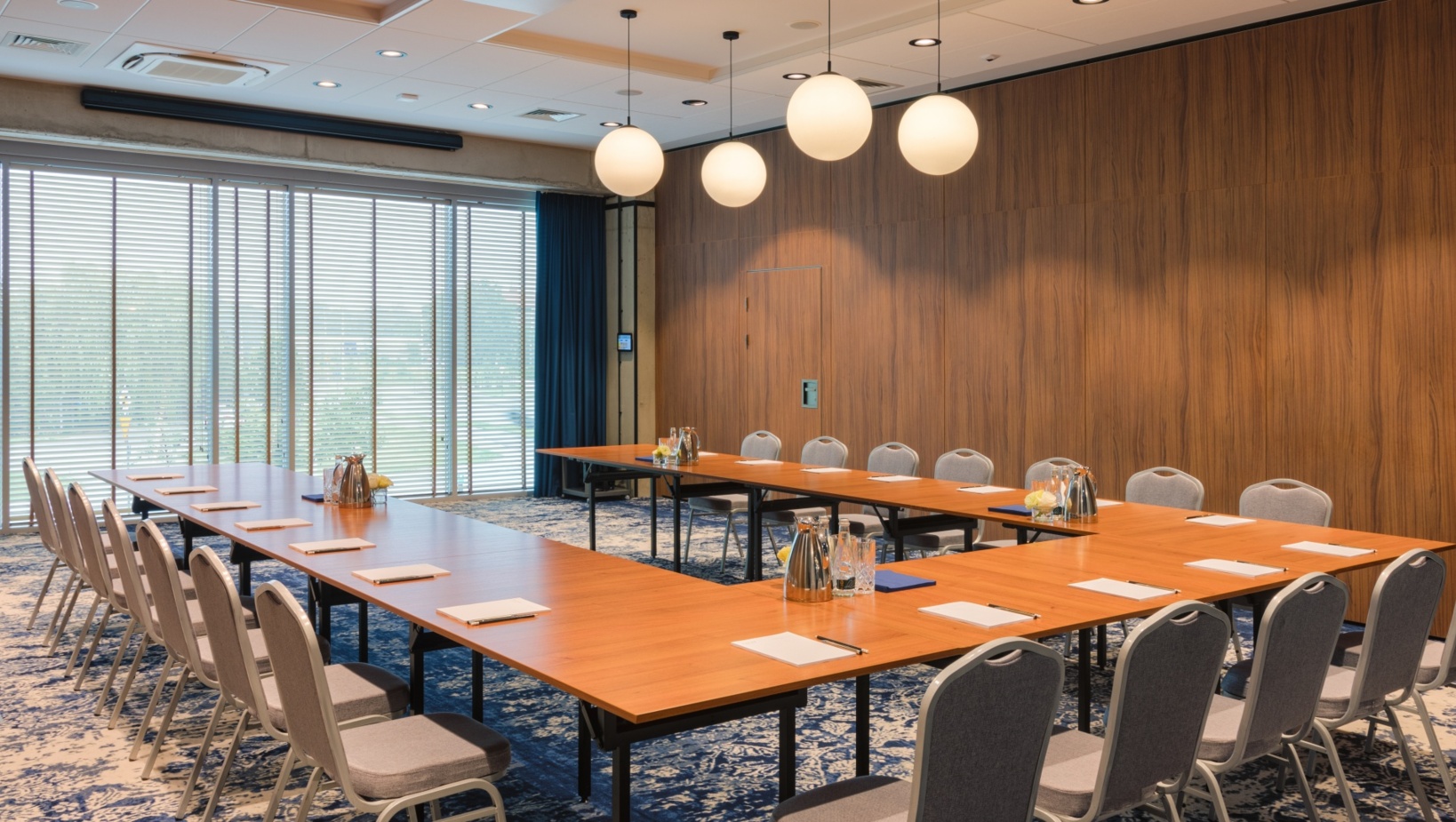 Nowoczesna sala konferencyjna z drewnianymi stołami w układzie U, wygodne krzesła i naturalne światło z dużych okien