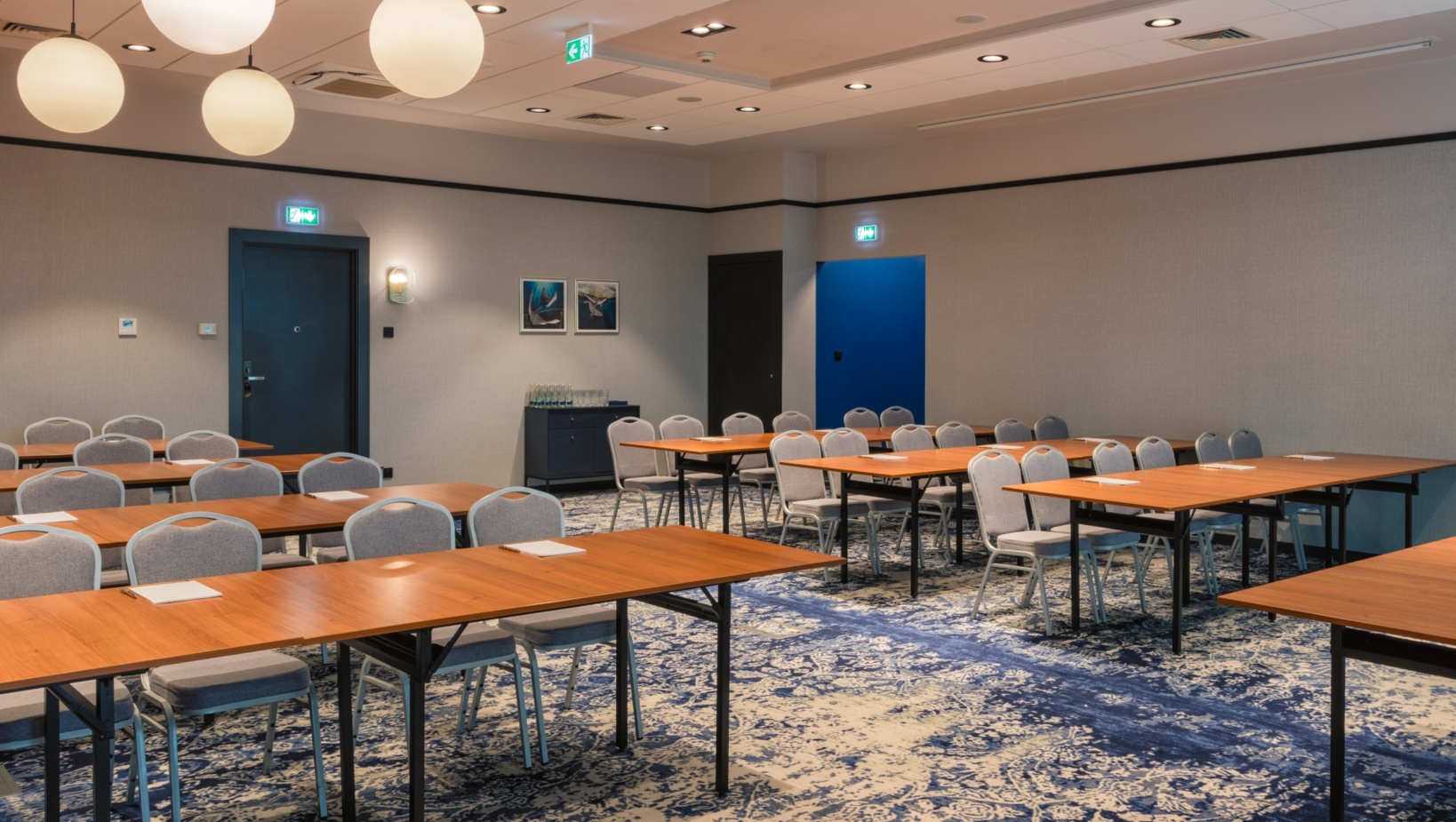 Nowoczesna sala konferencyjna z drewnianymi stołami, szarymi krzesłami i niebiesko-białym wzorzystym dywanem