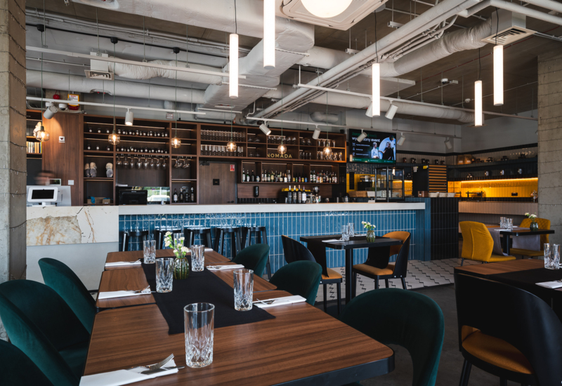 Modern hotel restaurant with blue-tiled bar, elegant tables, comfortable chairs, and warm ambient lighting creating inviting atmosphere.