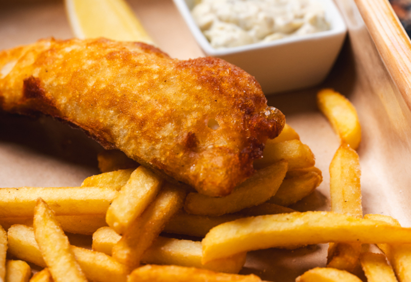 Crispy battered fish served with French fries, tartar sauce, and a lemon wedge on a wooden tray