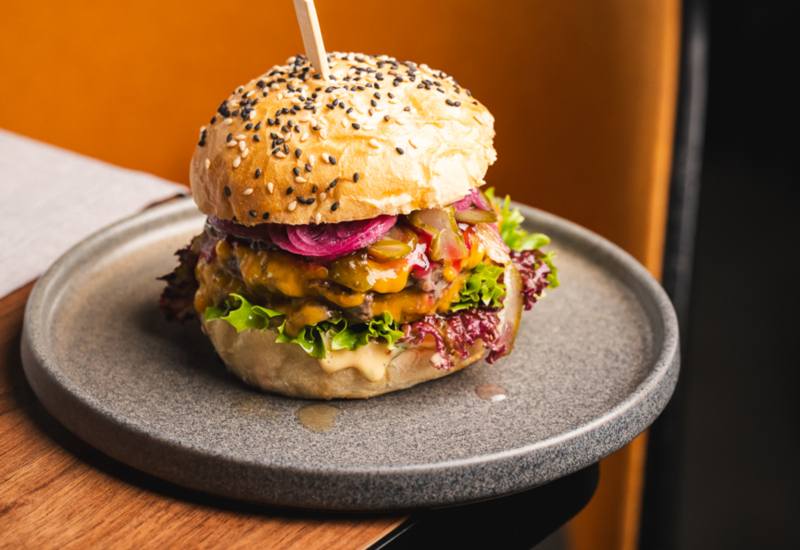 Juicy cheeseburger with lettuce, pickles, and sauce in a sesame-seed bun, served on a stylish plate in a modern restaurant.
