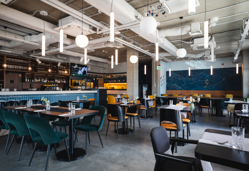 Modern hotel restaurant with a bar, comfortable green and mustard chairs, and minimalist pendant lighting for a relaxed dining atmosphere.