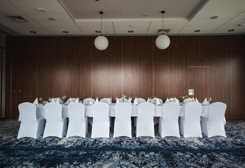 Elegant banquet table with white chair covers, fine table settings, and floral decorations in a modern conference room.