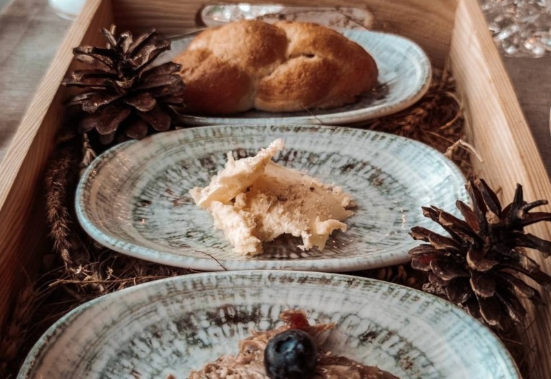 Rustic breakfast with bread, butter, and fruit on ceramic plates, decorated with natural pine cones on a wooden tray