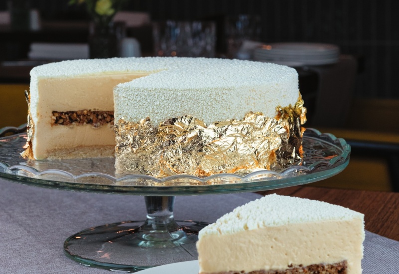 Luxury white dessert on glass stand with edible gold leaf and crunchy nut layer inside