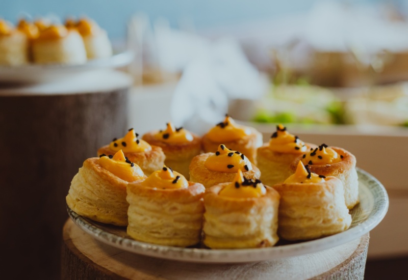 Plate of buttery puff pastry bites filled with creamy yellow topping and sprinkled with black sesame seeds, perfect for hotel breakfast