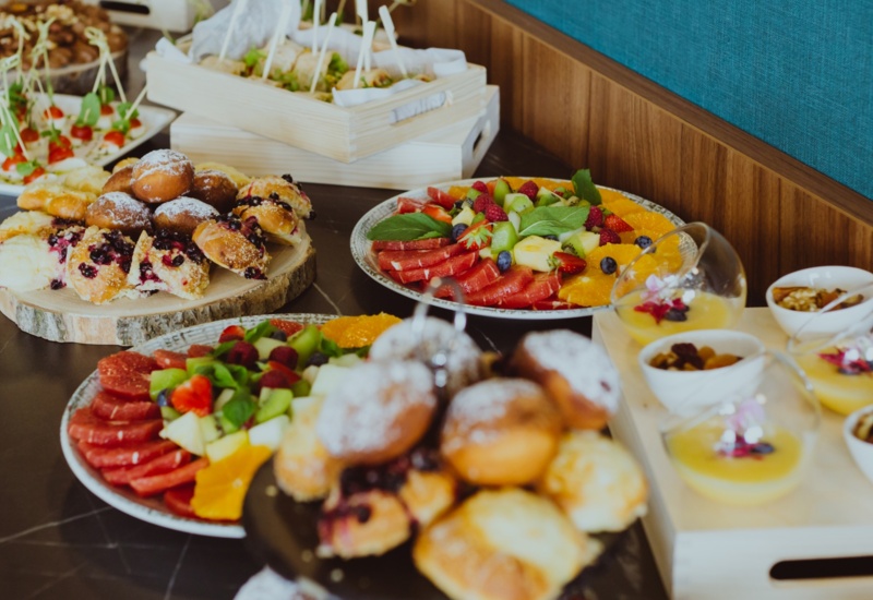 Buffet spread with assorted pastries, fresh fruit platters, and elegant desserts served on wooden and ceramic trays.