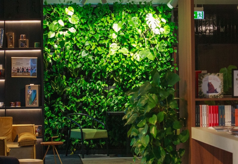 Cozy lounge area with lush green plant wall, modern seating, bookshelf with books and decorative items