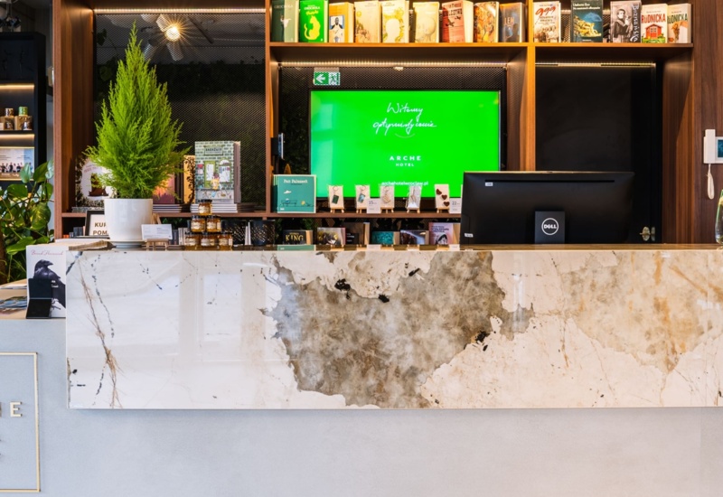 Hotel reception with marble countertop, green plant, and shelves with books and souvenirs in the background