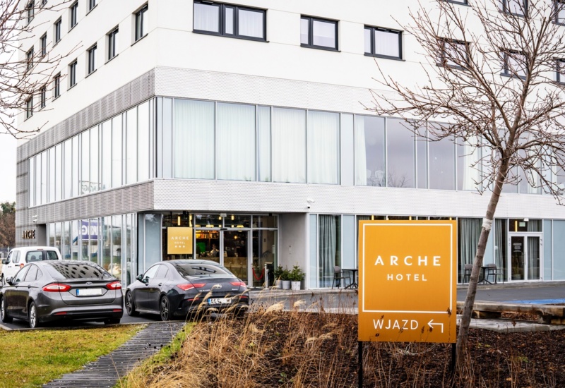 Modern Arche Hotel with large windows and outdoor parking, surrounded by urban greenery and bare trees