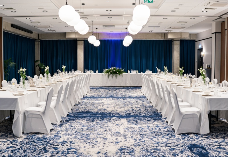 Elegant banquet hall with white tablecloths and chairs, floral decorations, and modern spherical ceiling lights