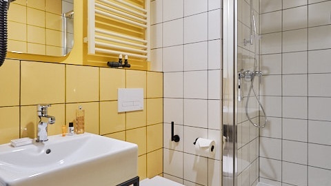 Modern hotel bathroom with yellow and white tiles, glass shower, sink, and mirror.