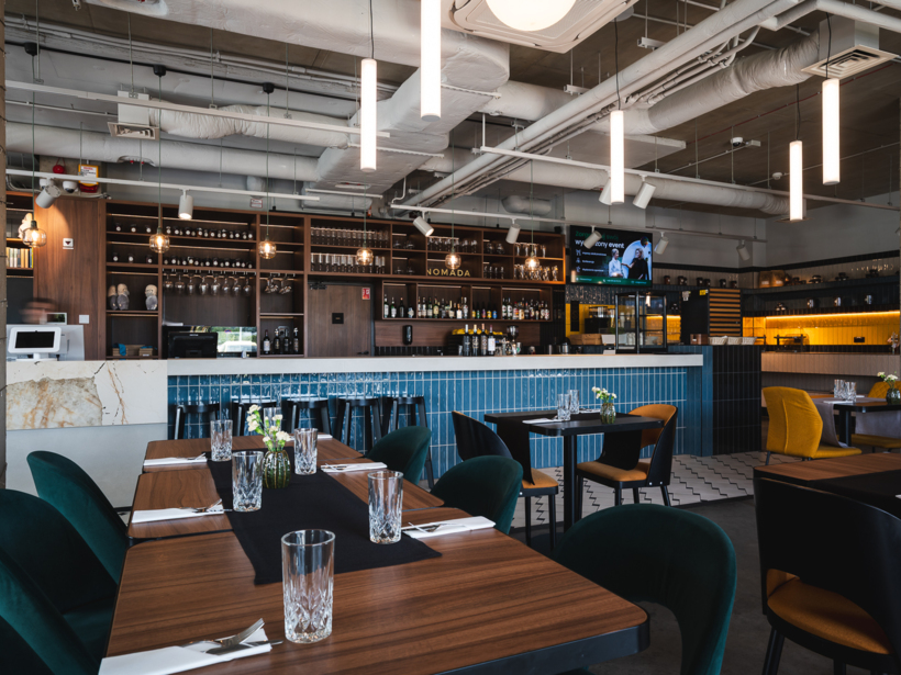 Nowoczesna restauracja hotelowa z barem wykończonym niebieskimi płytkami, eleganckimi stolikami i wygodnymi fotelami, przyjazna atmosfera.