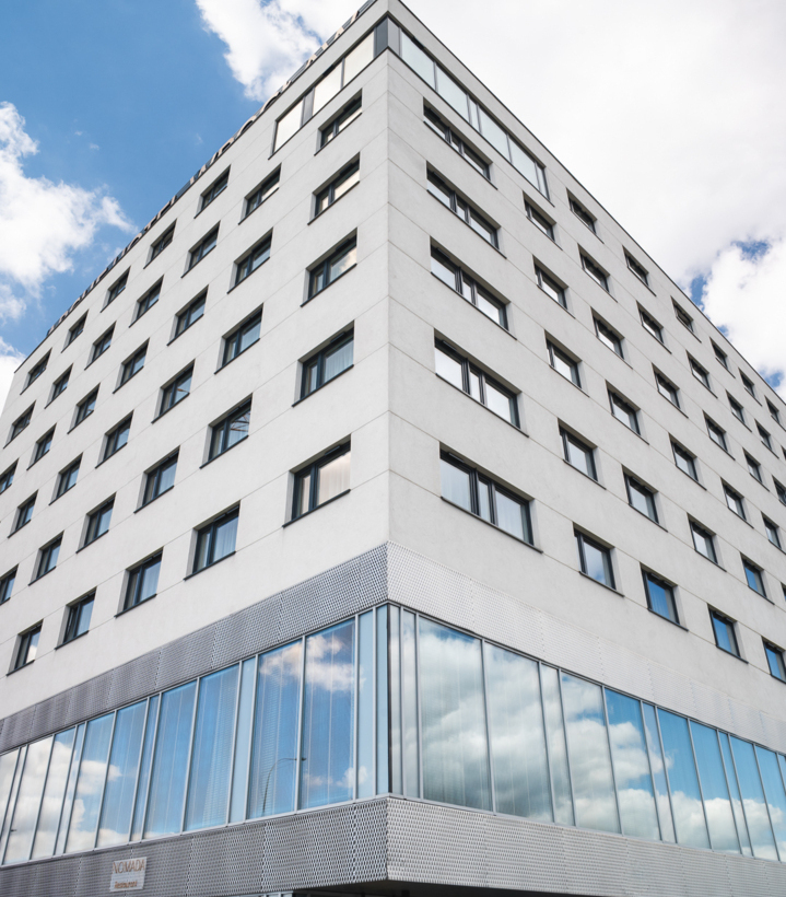 Modern white hotel building with large windows and glass ground floor under a cloudy sky.