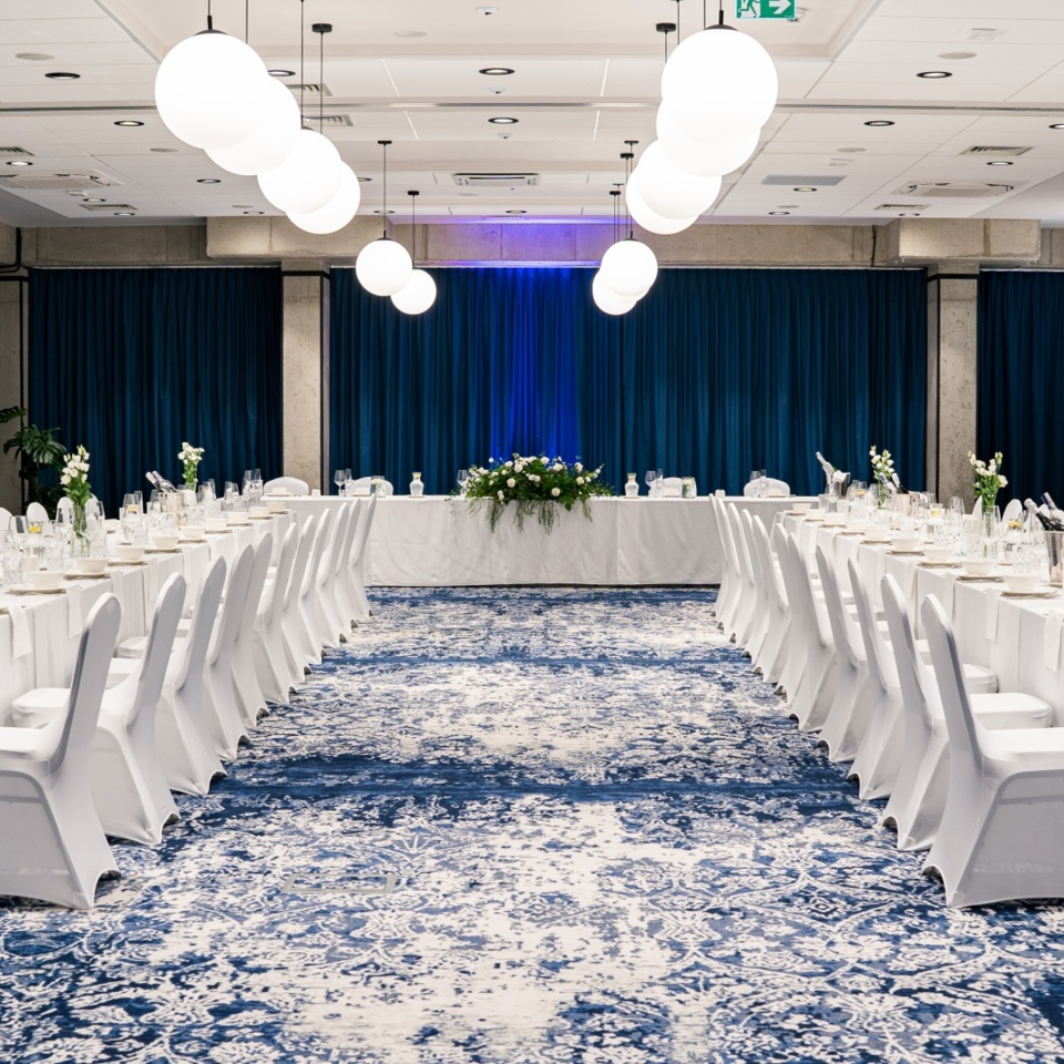 Elegancka sala bankietowa z białymi obrusami i krzesłami, dekoracjami kwiatowymi oraz nowoczesnym oświetleniem
