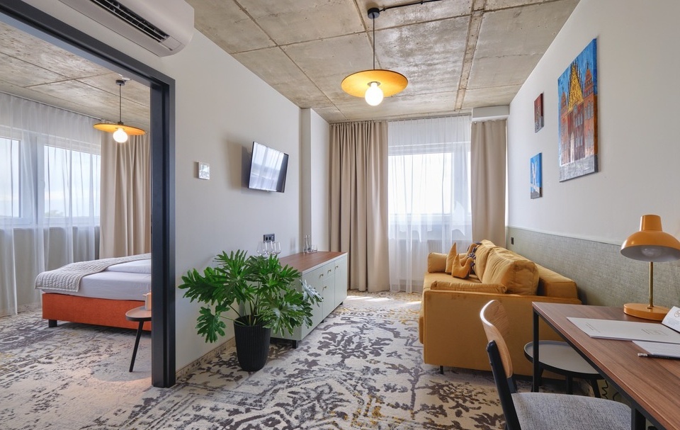 Modern hotel suite with a cozy living area, comfortable bedroom, large window, and decorative wall art.