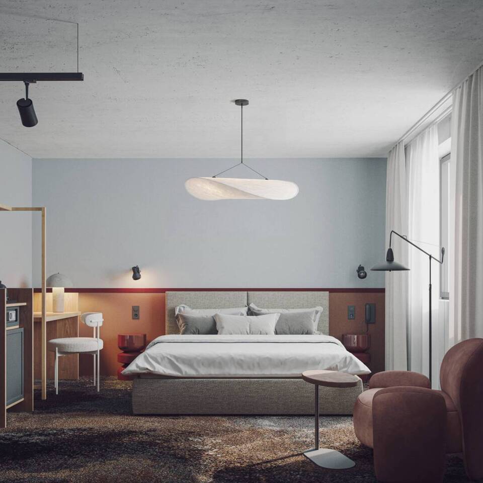 Modern hotel room with a large bed, plush armchair, desk, minimalist lighting, and sheer curtains by the window.