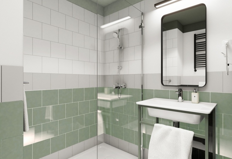 Modern hotel bathroom with walk-in glass shower, green-and-white tiles, wall-mounted shower, sink, mirror and folded towel