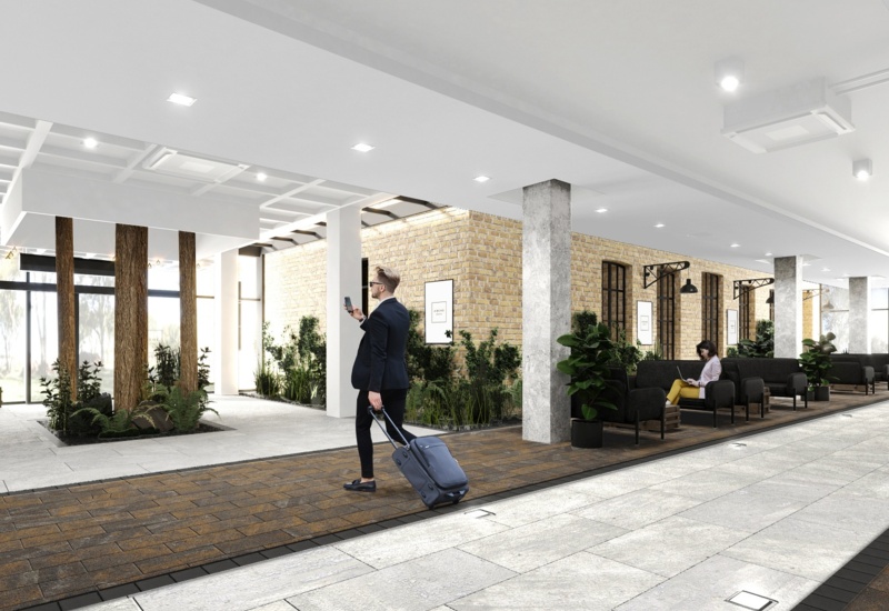 Modern hotel lobby with exposed brick, indoor plants, lounge seating and high ceilings; guest pulls suitcase, another uses a laptop.