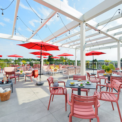 Spacious rooftop terrace with modern pink furniture, red umbrellas, and scenic views of lush greenery.