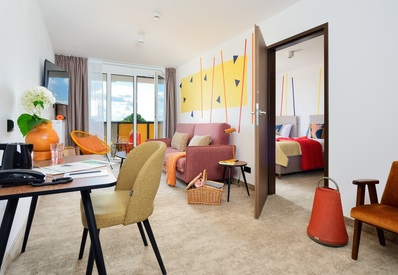 Nowoczesny apartament z salonem, balkonem z widokiem na zieleń, sypialnią, biurkiem i komfortowymi kolorowymi meblami