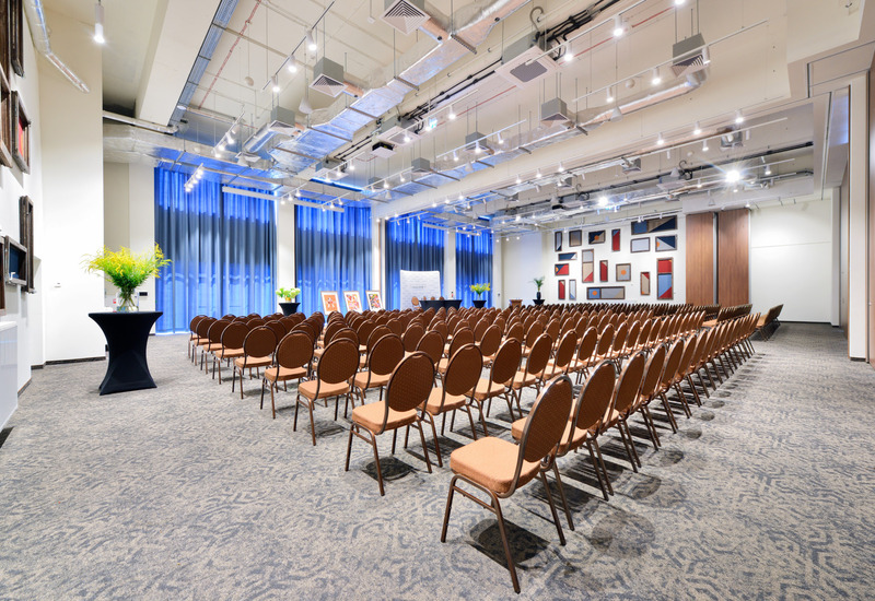 Spacious conference room with rows of chairs, modern lighting, and wall art, set up for a corporate or social event.