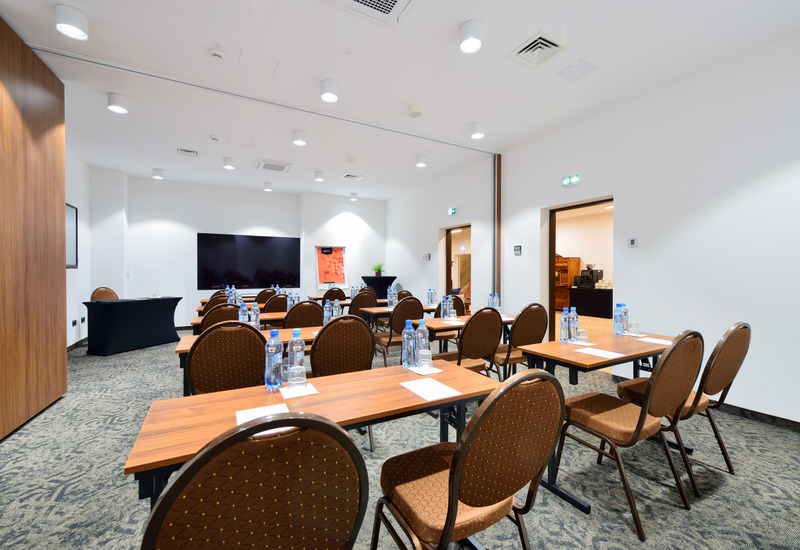 Modern conference room with wooden tables, brown chairs, and water bottles with notepads arranged on the tables.