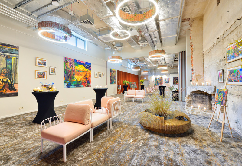 Spacious hotel lounge with pink sofas, modern circular lights, exposed walls, and vibrant paintings displayed on the walls.