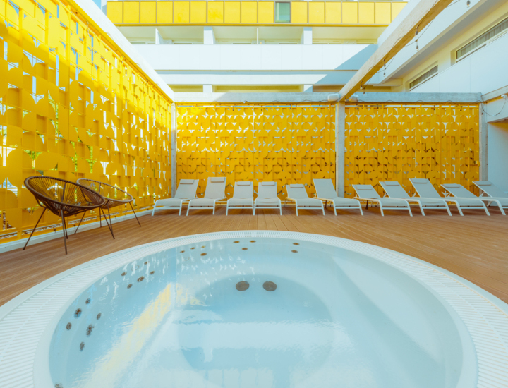 Hotel relaxation area with round jacuzzi, white loungers, and bright yellow decorative panels on the terrace.