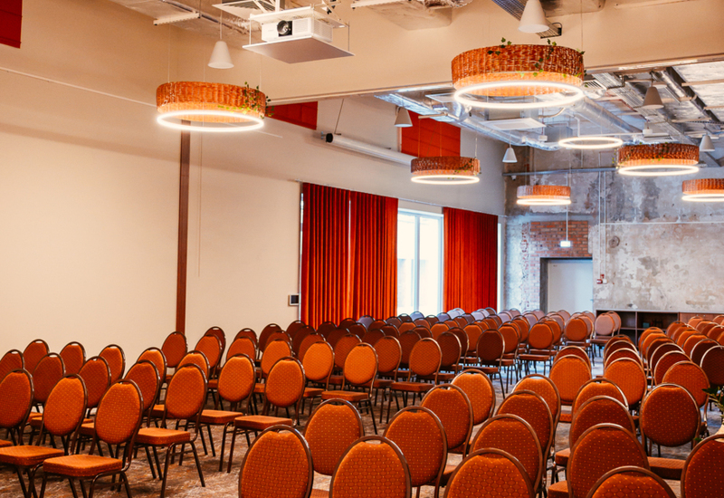 Conference room with rows of red chairs, modern circular lighting, and exposed industrial ceiling details