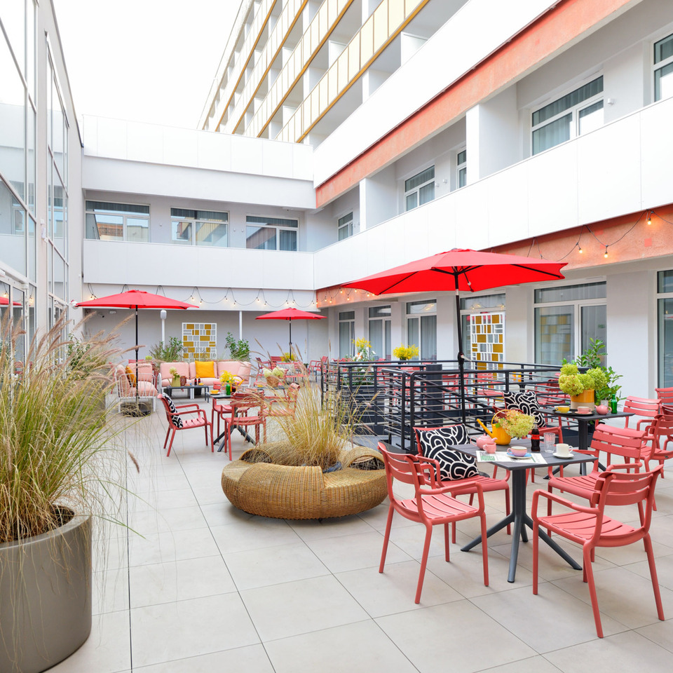 Modern hotel courtyard with red umbrellas, comfortable seating areas, and decorative plants for guest relaxation.