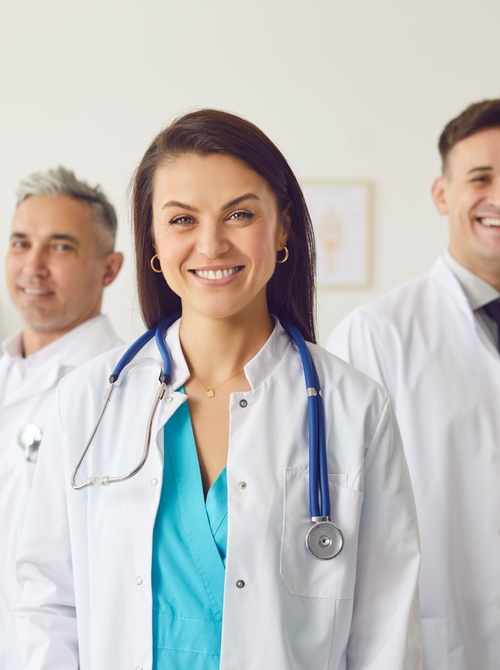 Uśmiechnięty zespół medyczny w białych fartuchach i uniformach, lekarka ze stetoskopem w jasnej przychodni