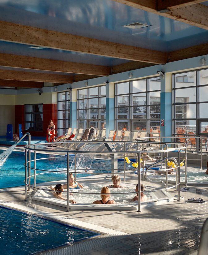 Kryty basen z jacuzzi i wodnymi dyszami, leżakami i dużymi oknami na taras; rodziny relaksują się w strefie spa.