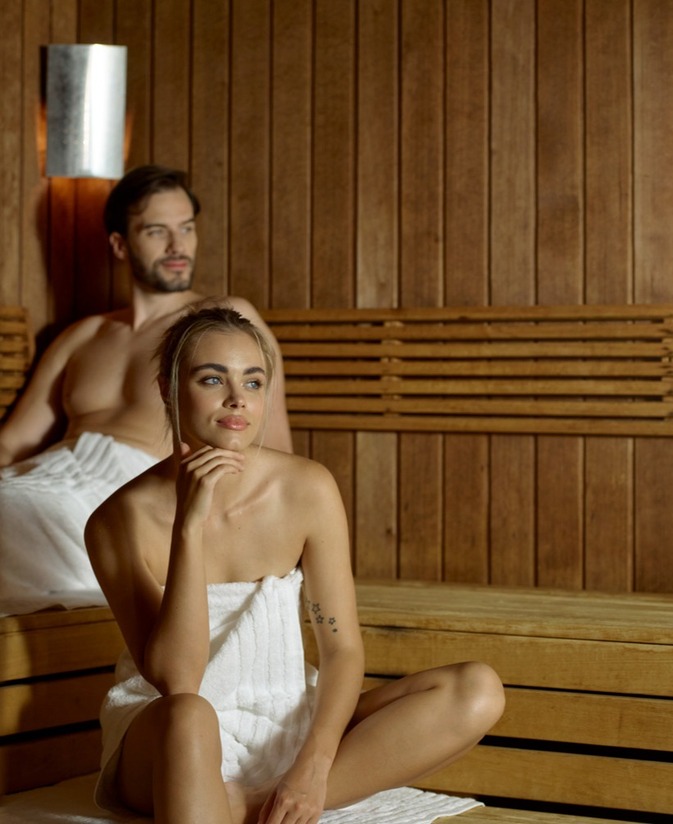 Para relaksuje się w drewnianej saunie hotelowej, miękkie oświetlenie ścienne, ręczniki i ławki, kojąca atmosfera spa.