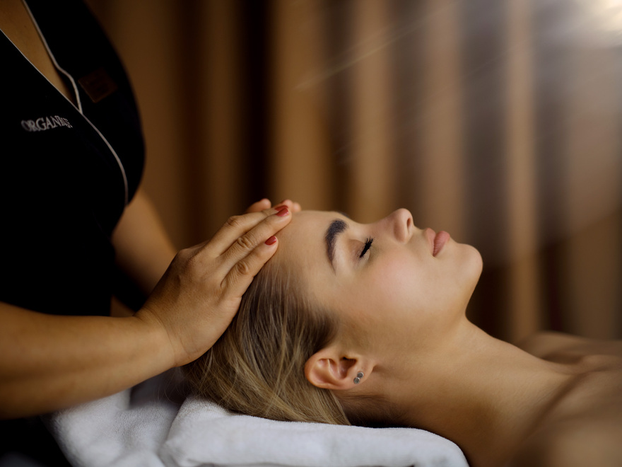 Gość korzysta z relaksującego masażu głowy i twarzy na łóżku spa, dłonie terapeuty, miękki ręcznik i ciepłe światło