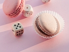 Two pink macarons on a pastel backdrop, one in a white paper cup, with scattered white dice as playful props