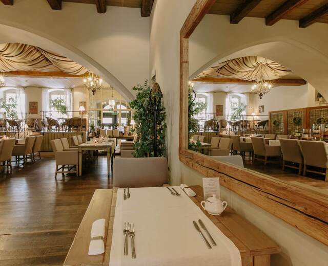 Elegancka restauracja hotelowa z łukowymi sklepieniami, żyrandolami, materiałowym baldachimem, odsłoniętymi drewnianymi belkami, lustrem i starannie nakrytymi stolikami.