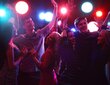 Group of young people dancing and enjoying a lively hotel party under colorful club lighting.