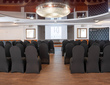 Elegant hotel conference room with rows of black-covered chairs, projector screen with Artis logo and a crystal chandelier.