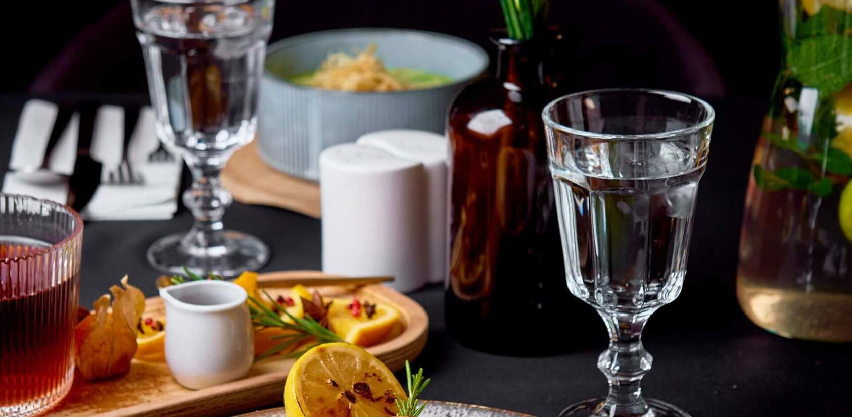 Seared salmon on vegetables with bright green purée, served at a set table with glassware, cutlery and a small vase of flowers