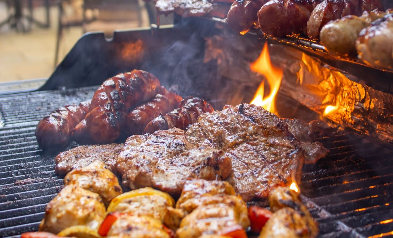 Steki, kiełbaski i szaszłyki z kurczaka na rozgrzanym grillu, dymiący ogień i rozmyte stoliki tarasowe