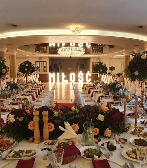 Luksusowa sala bankietowa z długimi stołami udekorowanymi kwiatami, świecami i elegancką zastawą na romantyczne przyjęcie