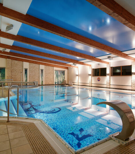 Przestronny kryty basen hotelowy z mozaikową podłogą, drewnianymi belkami na suficie i relaksującą atmosferą.