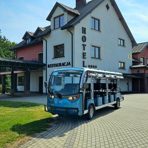 Open-air electric hotel shuttle parked by a multi-story hotel entrance with covered driveway, restaurant sign and spa building.