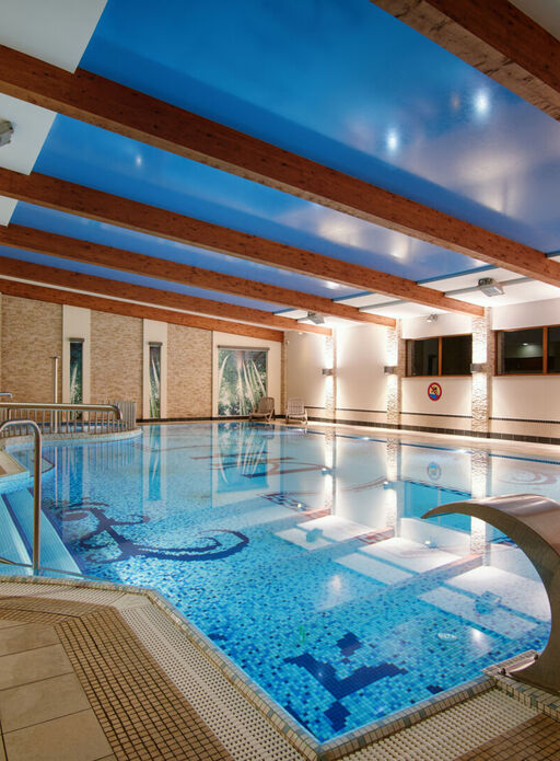 Przestronny kryty basen hotelowy z mozaikową podłogą, drewnianymi belkami na suficie i relaksującą atmosferą.