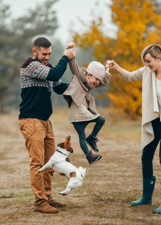 Rodzina bawi się z dzieckiem i psem na jesiennej polanie w otoczeniu kolorowych drzew